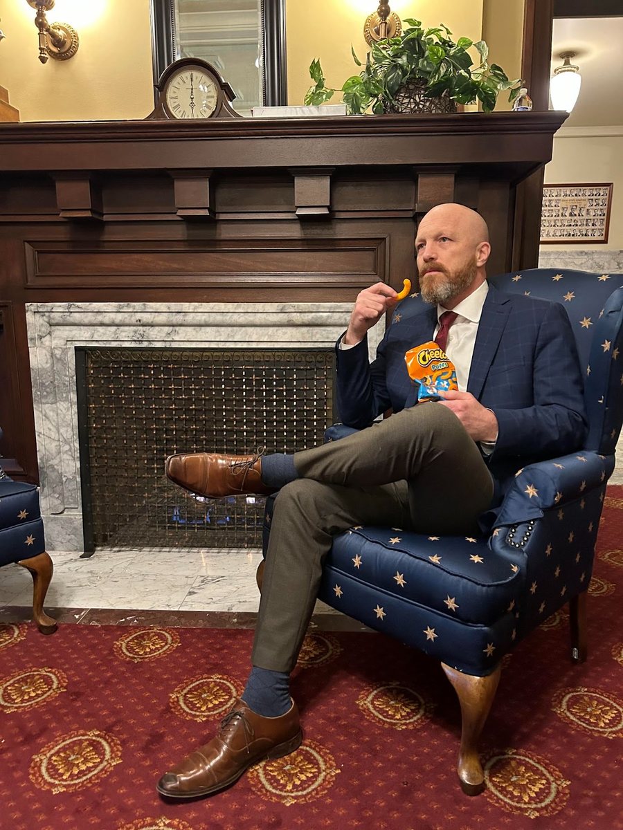 Brian Lenney in a wingback chair at the Idaho Capitol eating Cheetos